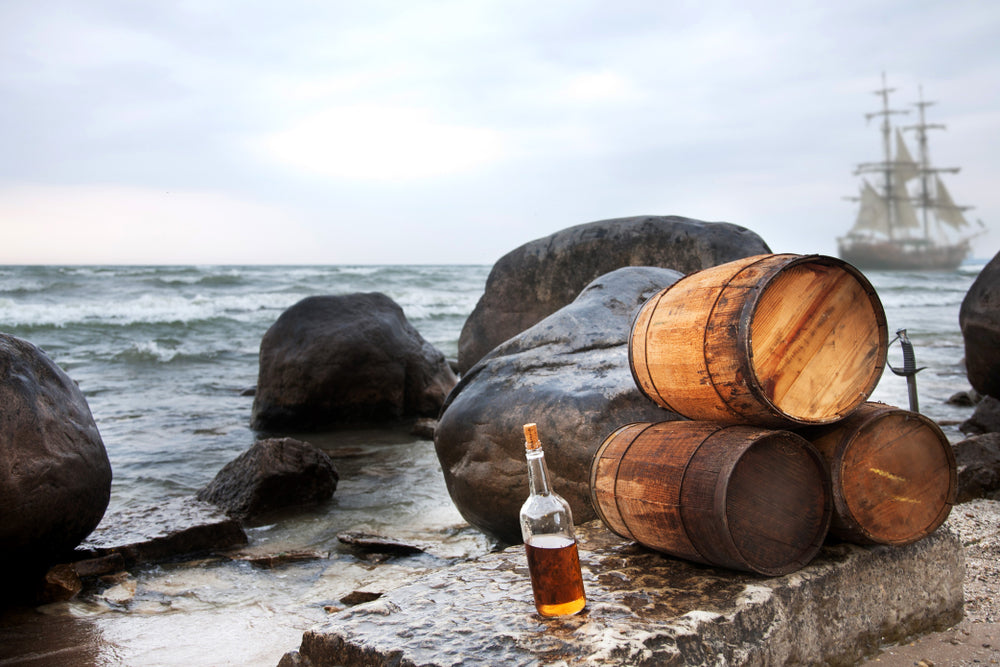 Rum Bottle and Rum Barrels with Pirate Ship in Background | Blind Pig Drinking Co.